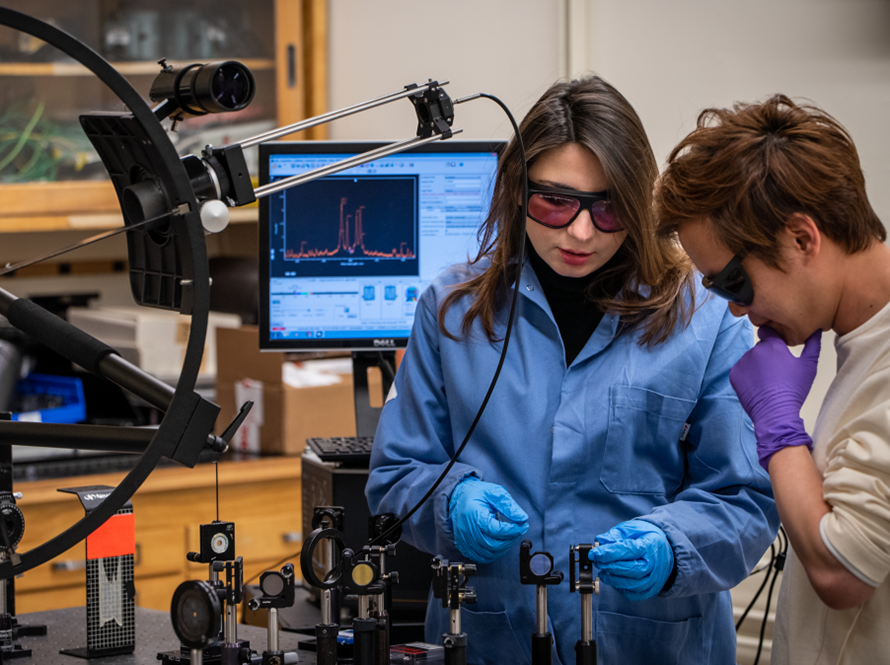 two researchers with safety googles looking down at lens