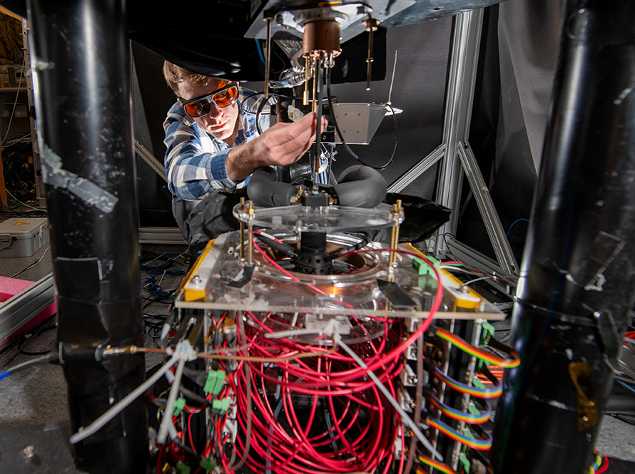 researcher with orange lens glasses looking closely at wires in scientific equipment