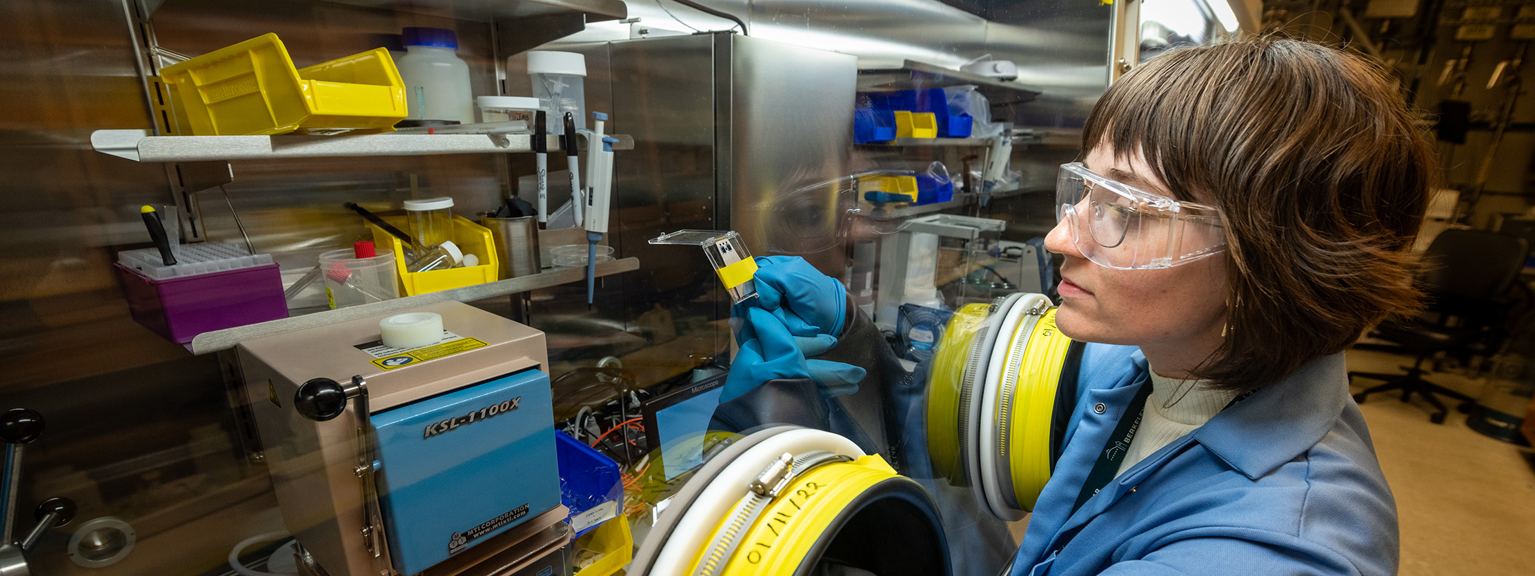 researcher with safety glasses checks scientific samples that are behind safety glass